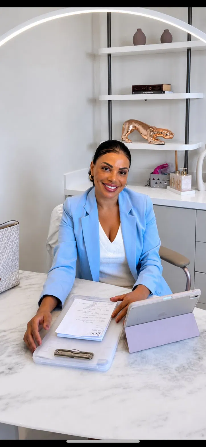 Fabiana Fiume de blazer azul claro sentada à mesa de mármore com prancheta e tablet